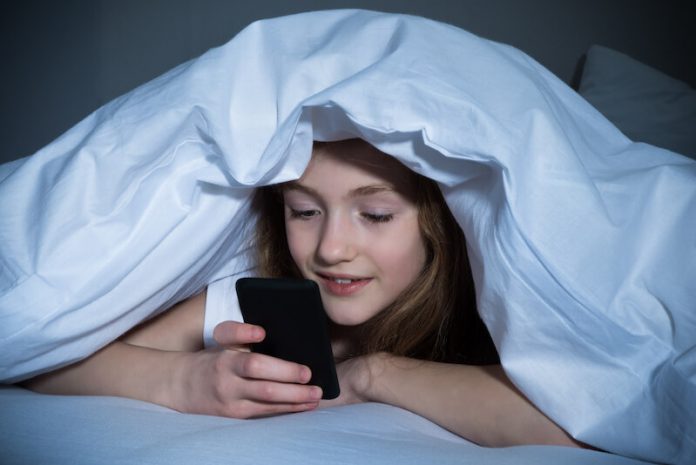 Une collègienne consultant son smartphone en cachette durant la nuit.