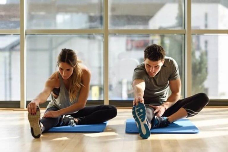 Un homme et une femme qui s'étirent avant une séance de sport pour éviter d'éventuelles courbatures.