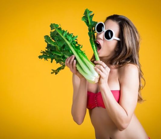 Une jeune femme faisant semblant de manger des légumes pour perdre des kilos avant le retour à la plage.