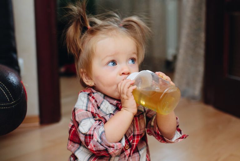 une petite fille boit du soda dans un biberon