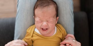 un bébé pleure dans son berceau et deux mains le secoue