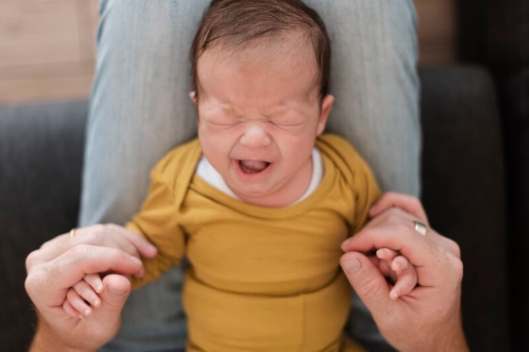 un bébé pleure dans son berceau et deux mains le secoue
