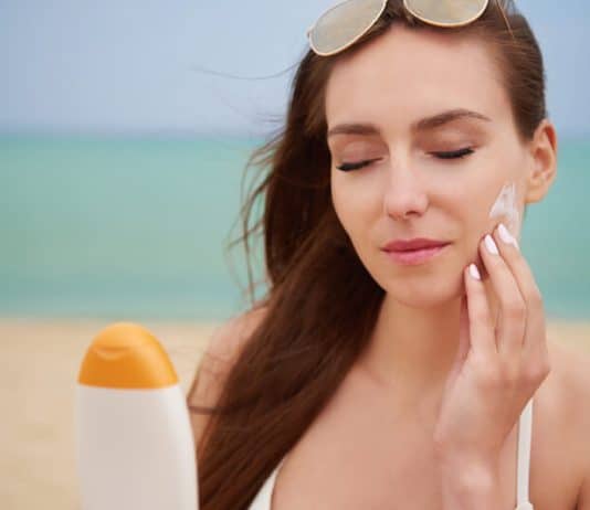 Une femme applique de la crème solaire sur le visage pour éviter les coups de soleil et protéger sa peau.