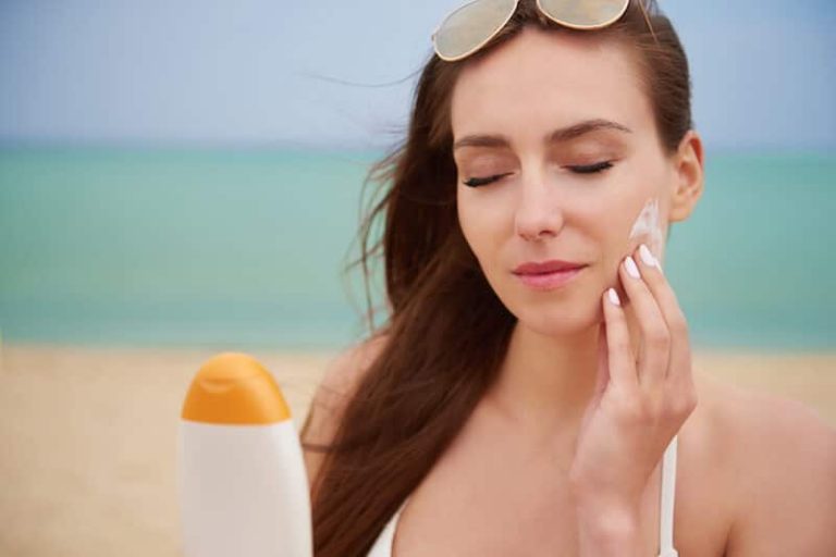 Une femme applique de la crème solaire sur le visage pour éviter les coups de soleil et protéger sa peau.