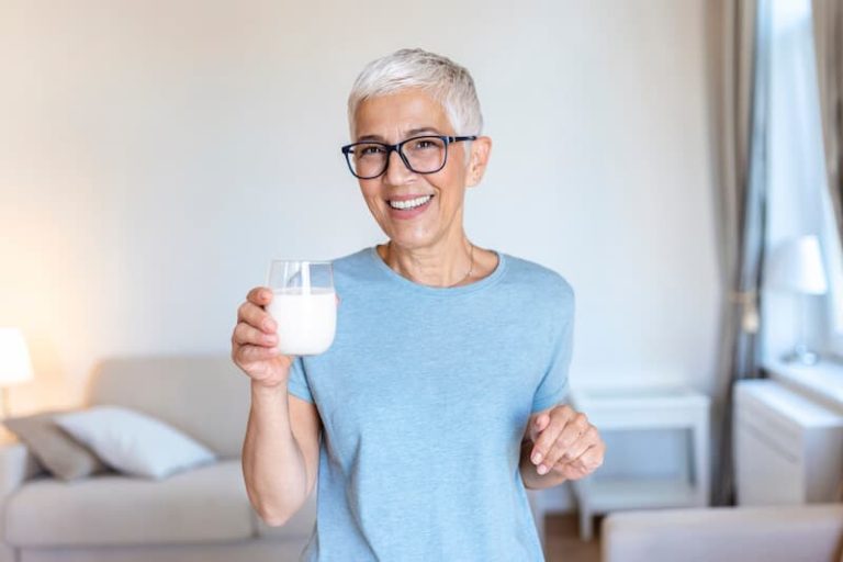 Femme senior buvant un verre de lait riche en calcium.