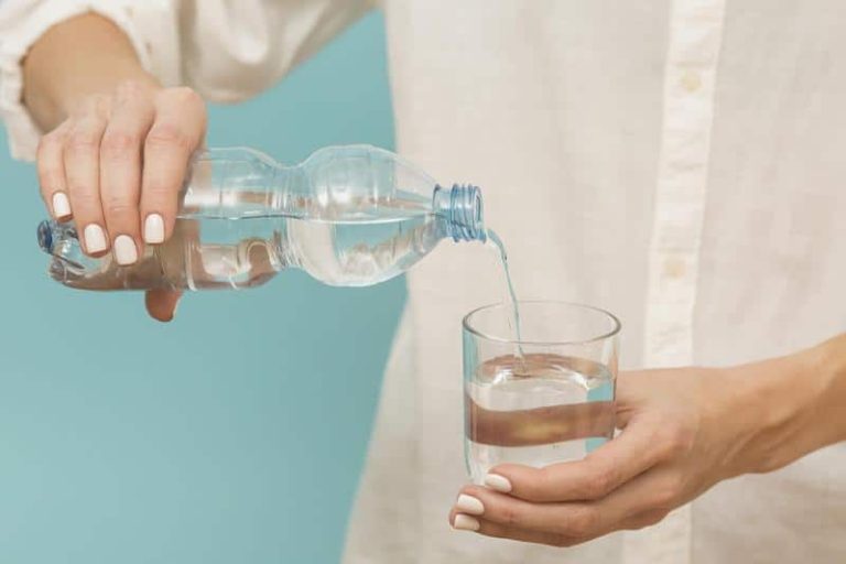 Une femme verse de l'eau plate ou de l'eau gazeuse dans un verre.