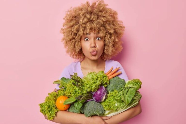 Une femme avec les bras chargés de légumes.