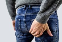Un homme en jean se gratte une zone de démangeaison au niveau de l'anus.