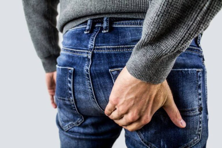 Un homme en jean se gratte une zone de démangeaison au niveau de l'anus.