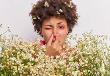 Une femme allergique se bouche le nez en présence du pollen des fleurs devant elle.