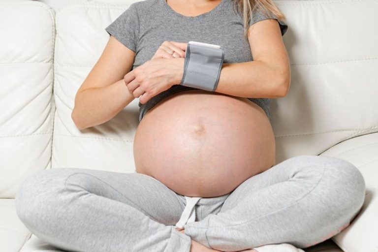 Une femme enceinte utilise un tensiomètre pour mesurer elle-même sa tension artérielle.