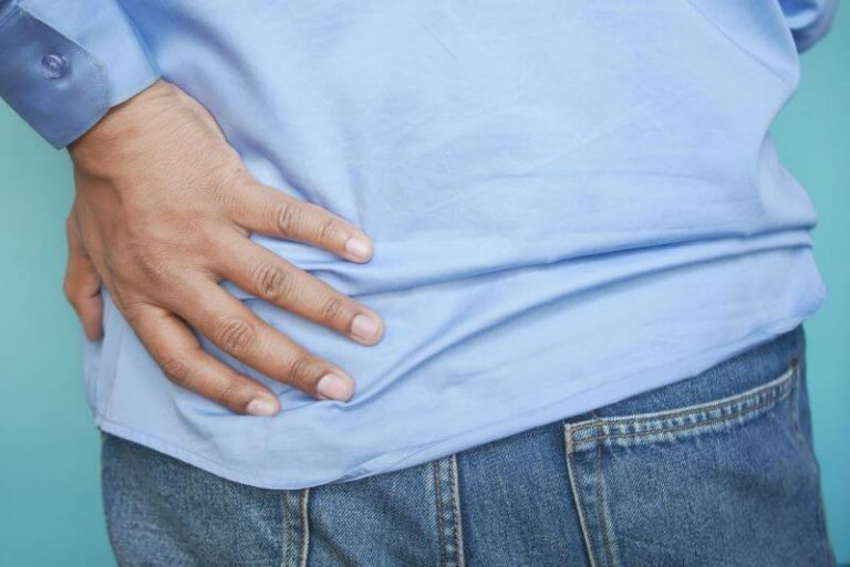 Un homme se tient le haut de la fesse en raison de la douleur causée par un kyste sacro-coccygien.
