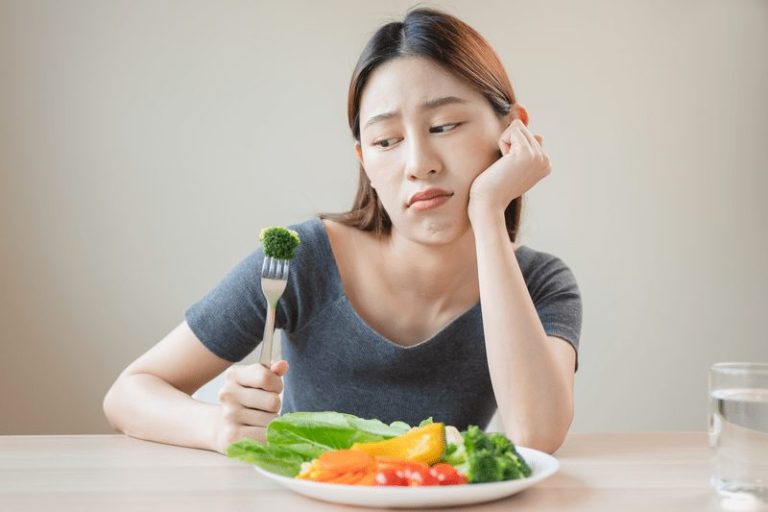 Une femme qui mange des légumes avec dégoût qu'elle a du cholestérol.