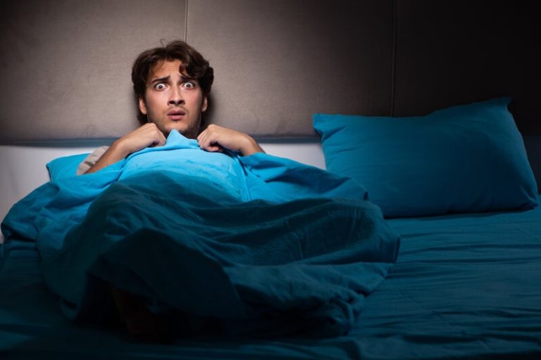 Un homme dans son lit en pleine nuit qui se réveille apeuré à cause de cauchemars à répétition.