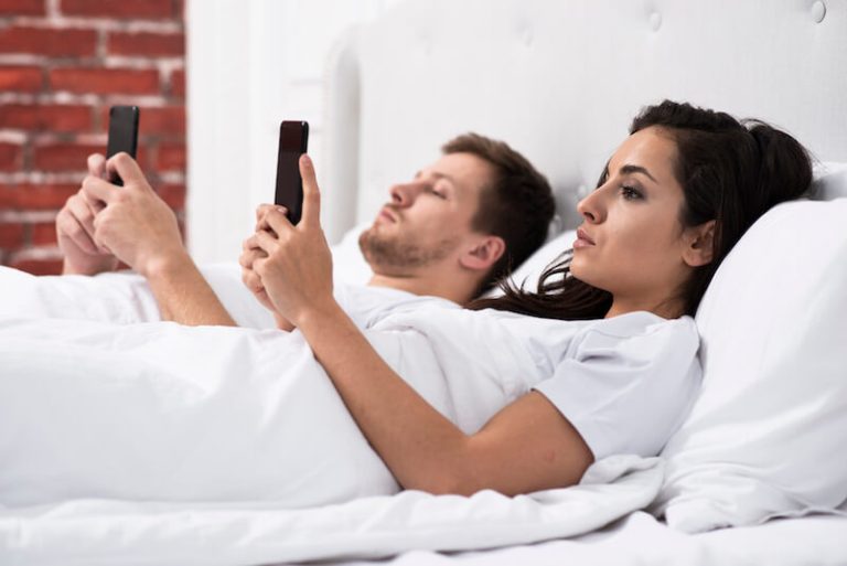 Un jeune couple avec des écrans au lit, symbole de la récession sexuelle qui touche la France.