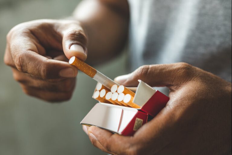 Un homme qui sort une cigarette de son paquet pour fumer.