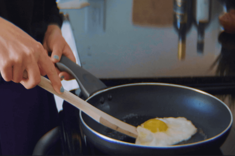 Une femme cuisine un œuf au plat dans une poêle potentiellement contaminée par les PFAS.