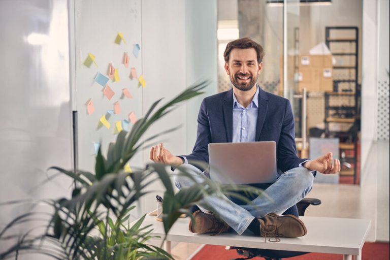 Un homme heureux, assis en tailleur sur son bureau, en bonne santé au travail.