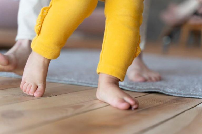 Un bébé apprend à marcher accompagné de son parent.