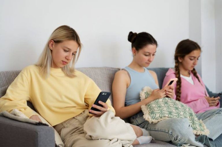 Trois adolescentes sont sur un canapé, les yeux rivés sur leurs smartphones.