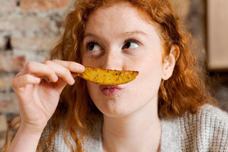 Une jeune femme tient une pomme de terre cuite dans la main.