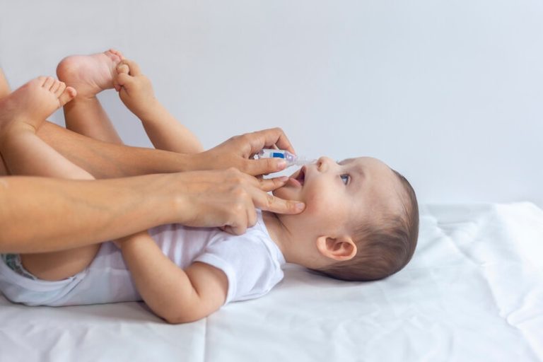 Un bébé sur une table à langer avec sa maman qui lui nettoie le nez au sérum phy.