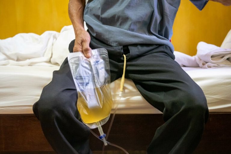 Un homme assis sur son lit avec une sonde urinaire qu'il tient dans sa main.