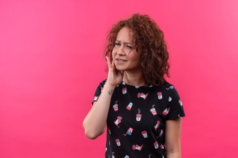 Une femme se tient la joue, la douleur de la rage de dent étant insupportable.