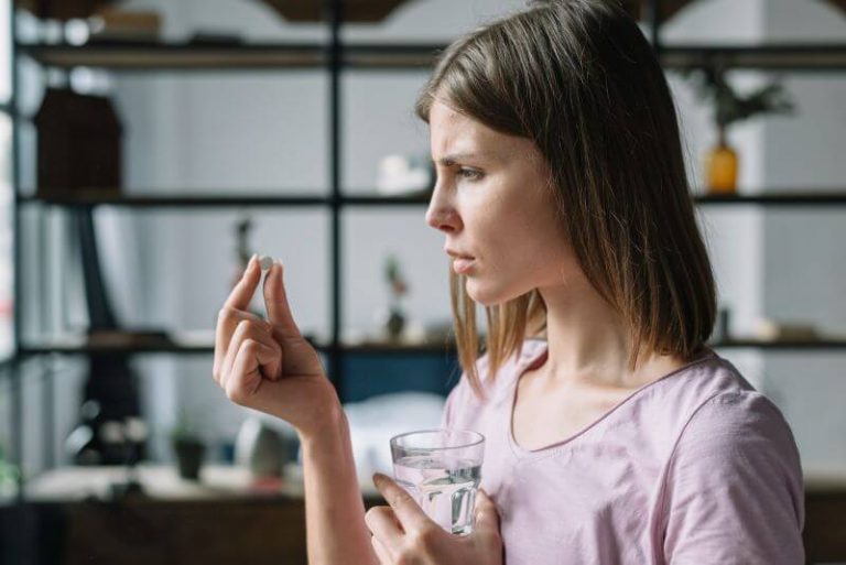 Une femme tient une pilule contraceptive dans une main et un verre d'eau dans l'autre.