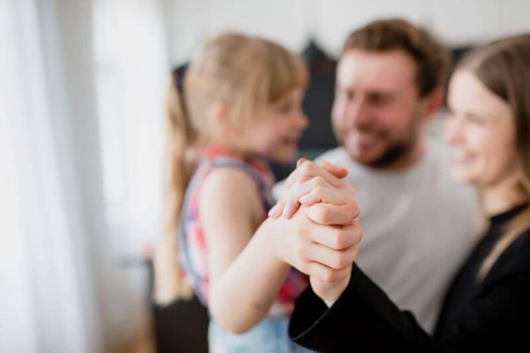 Deux parents sourient en tenant la main de leur jeune fille.