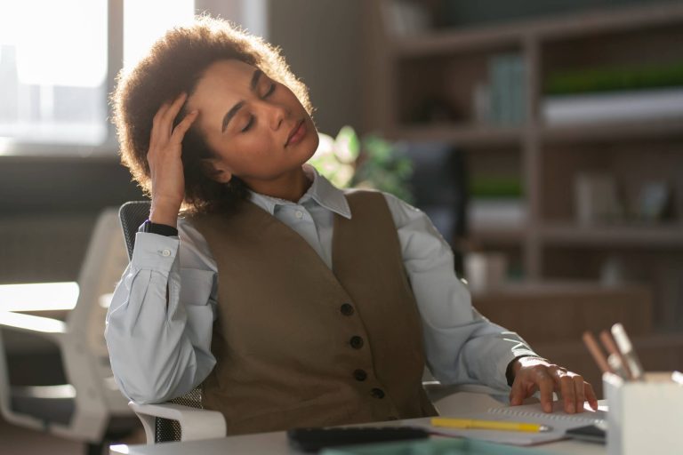 Une femme au travail se tient la tête, visiblement stressée.