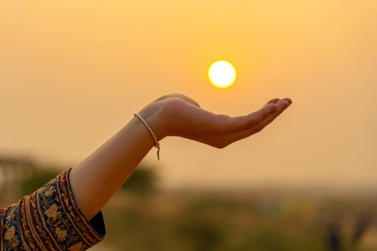 La silhouette d'ue main de femme en train de porter le soleil pendant le coucher de soleil.