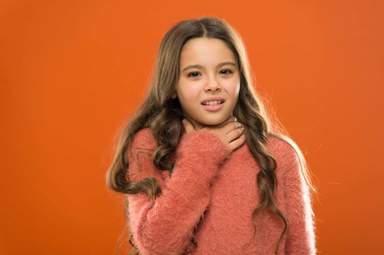 Une jeune fille se tient la gorge à cause de la douleur.