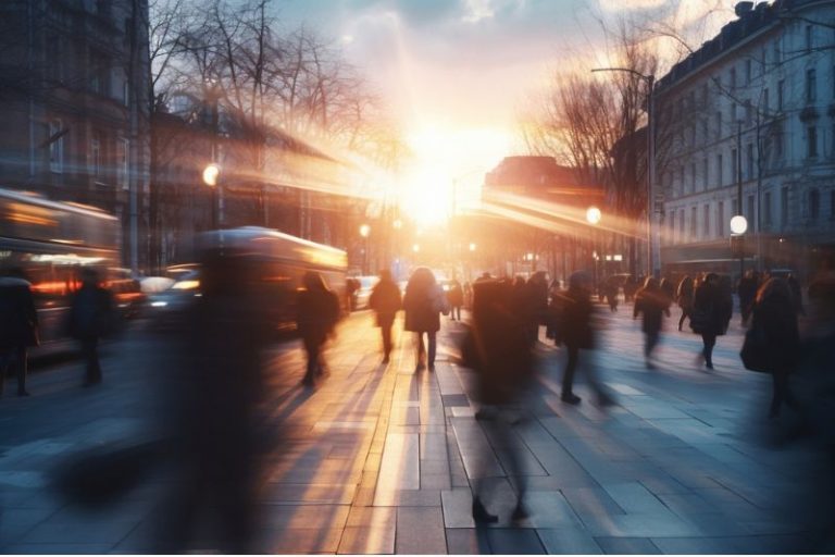 Des passants se baladent en ville avec un coucher de soleil en fond.