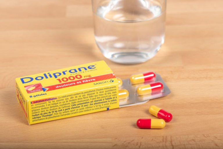 Une boîte de Doliprane posée sur une table avec un verre.