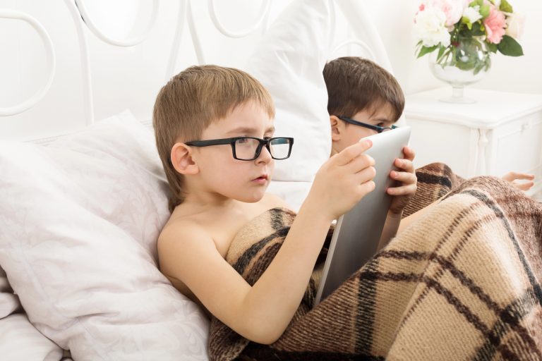 Un enfant avec des lunettes, souffrant de problèmes de vue, les yeux rivés sur les écrans.