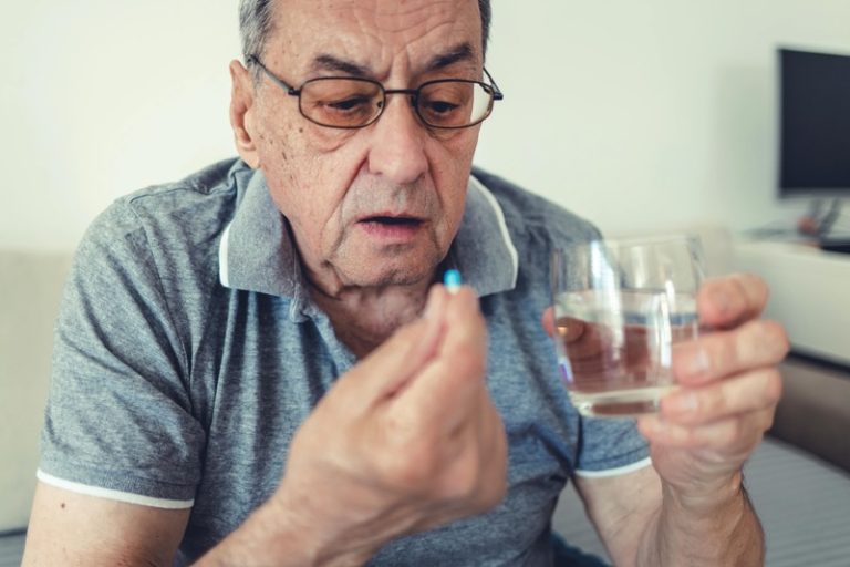 Un homme avec un verre d'eau à la main, prenant ses antibiotiques.