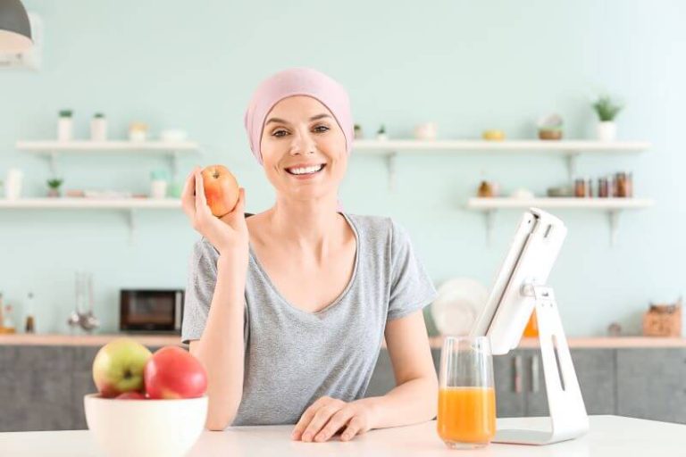 Une femme en plein traitement de chimiothérapie sourit et prépare des repas sains dans sa cuisine.