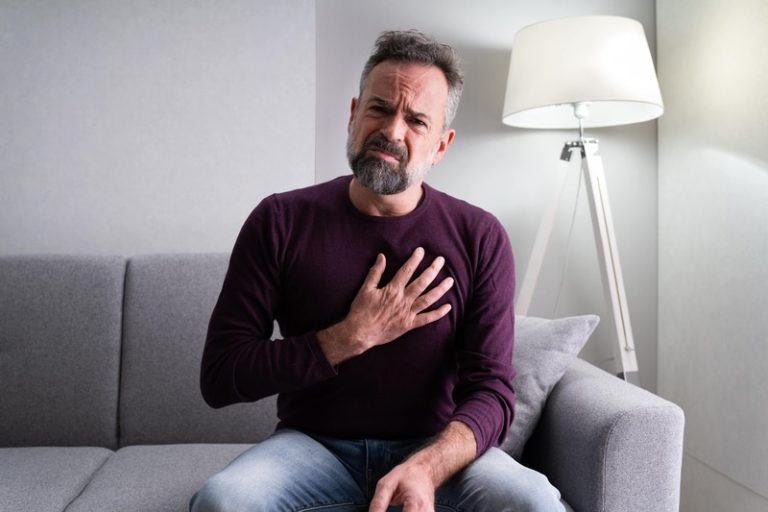 Un homme assis sur un canapé avec la main posé sur le coeur car il risque un infarctus à cause de son taux de cholestérol.