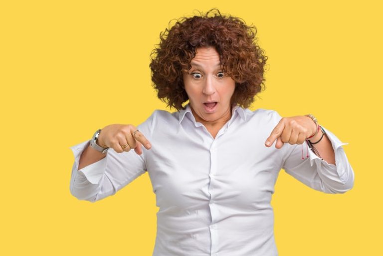 Une femme étonnée des symptômes liés à la ménopause poitnant le regard et les mains vers ses parties intimes.