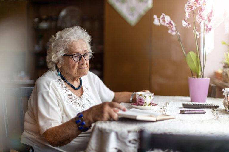 Une femme âgée assise seule à table avec une tasse de thé.