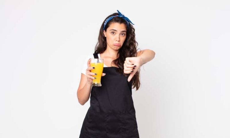 Une femme montrant le pouce vers le bas et tenant un verre de jus d'orange pour montrer que les jus de fruits ne sont pas bons pour la santé cardiovasculaire.