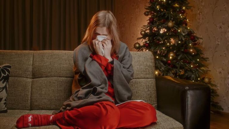 Une jeune femme sur son canapé, à côté de son sapin infesté de microbes, en train de se moucher.