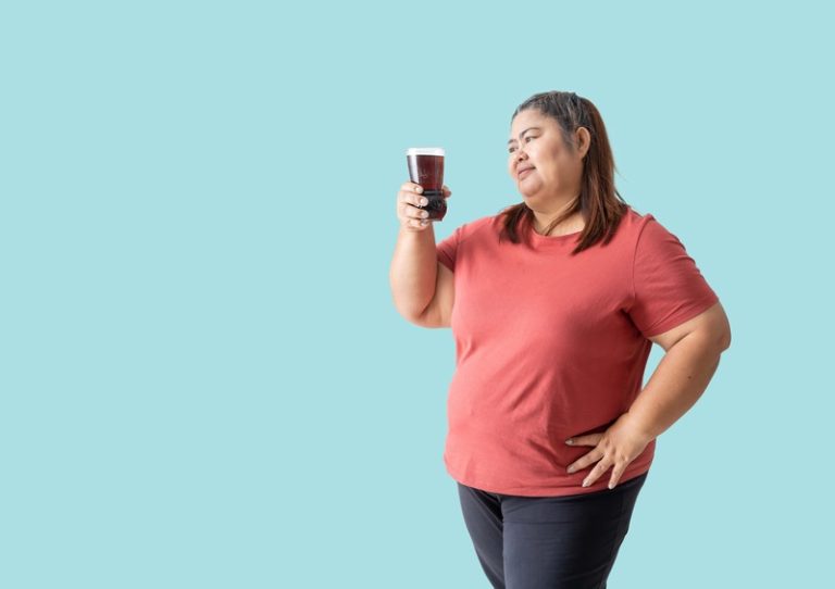 Une femme obèse qui s'interroge sur les dangers des sodas avec un verre plein de coca à la main.