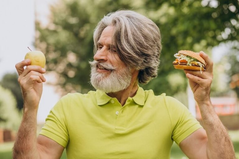 Un homme âgé hésite entre une pomme et un hamburger.
