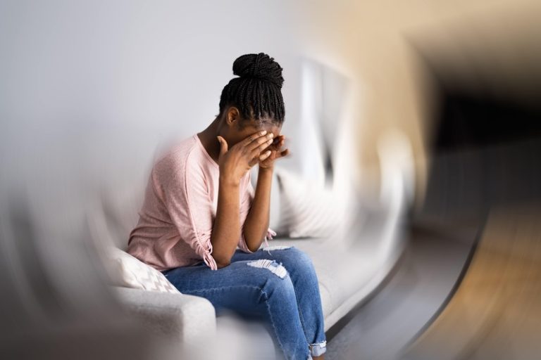 Une femme assise sur son canapé en train d'avoir une violente migraine.