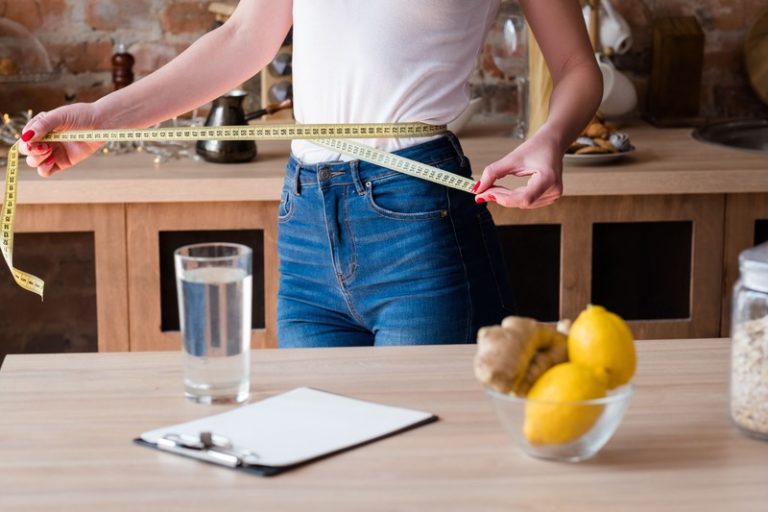 Une femme dans sa cuisine en train de mesurer son tour de taille pour voir si sa consommation de gingembre l'a aidée à perdre du poids.