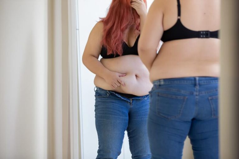 Une femme obèse, sans t-shirt, se regardant dans le miroir.