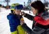Sports d’hiver : le soleil encore plus dangereux qu’à la plage Une maman qui met de la crème solaire sur le visage de son fils pour le protéger des UV du soleil d'hiver pendant les vacances au ski.