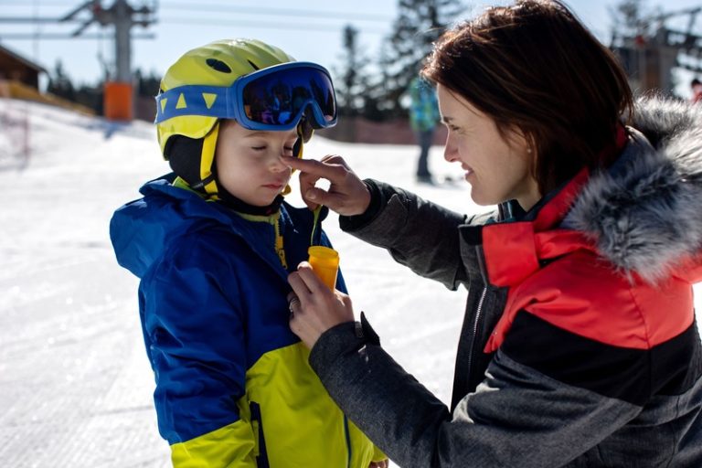 Une maman qui met de la crème solaire sur le visage de son fils pour le protéger des UV du soleil d'hiver pendant les vacances au ski.